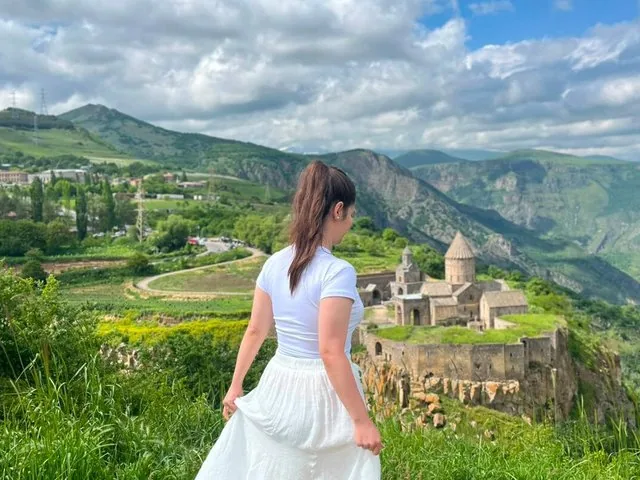 Woman looking at Tatev Monastery in a lush green valley.