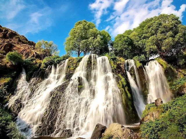 Beautiful wide view of Shaki Waterfall flowing over rocky, moss-covered terrain.