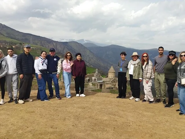 Group of tourists posing together overlooking the historic Tatev Monastery.