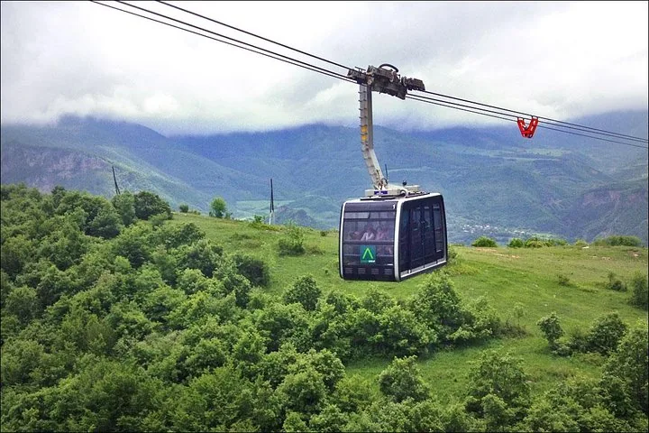 Wings of Tatev cable car traveling over a forested landscape.