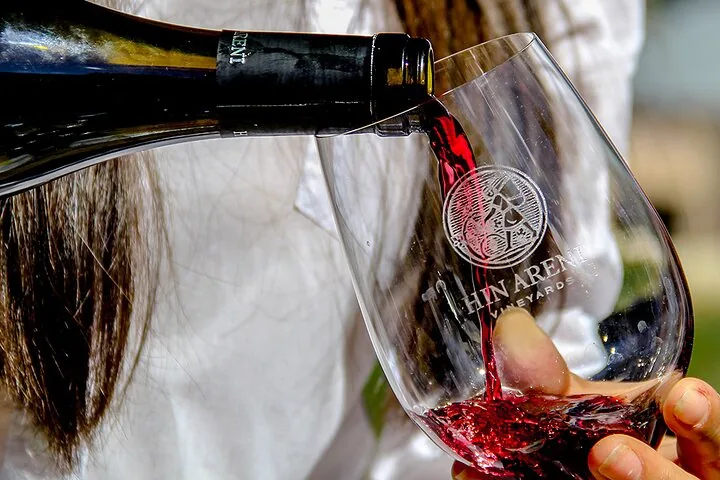 Red wine being poured from a bottle into a branded glass.